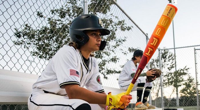 Baseball player in uniform holding a bat on a field with trees in the background